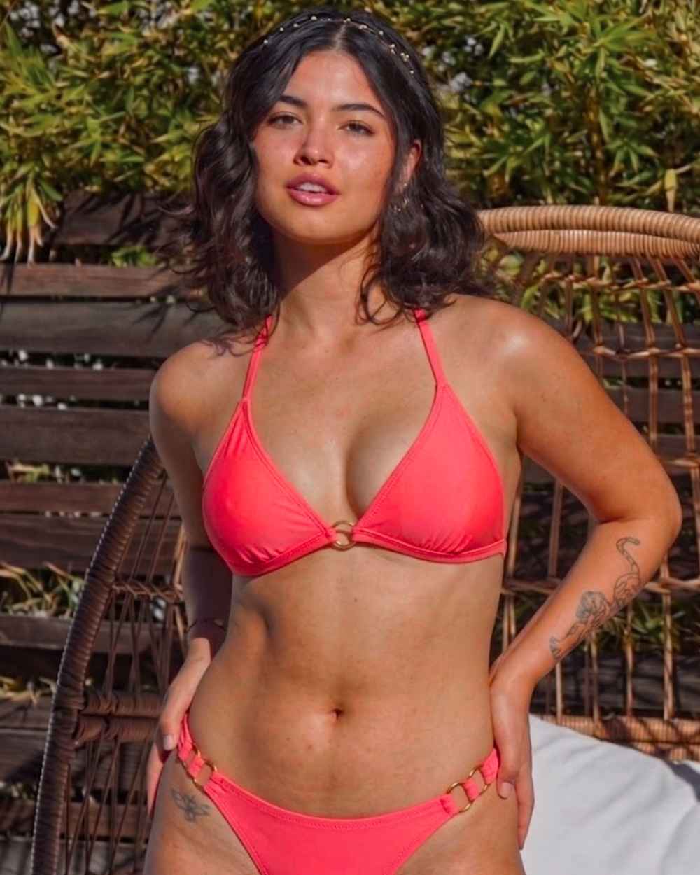 Woman wearing a red bikini standing outdoors with greenery in the background